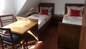 Ein kleiner, gemütlicher Raum mit zwei Einzelbetten, einem Holztisch und einem Stuhl.