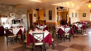 A restaurant with multiple tables and chairs, a kitchen area, and a restroom visible in the background.