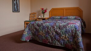 A hotel room with a bed, a chair, a nightstand with a vase of flowers, and a framed picture on the wall.