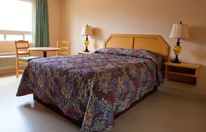 A hotel room with a large bed, two bedside tables with lamps, a chair, and a small table.