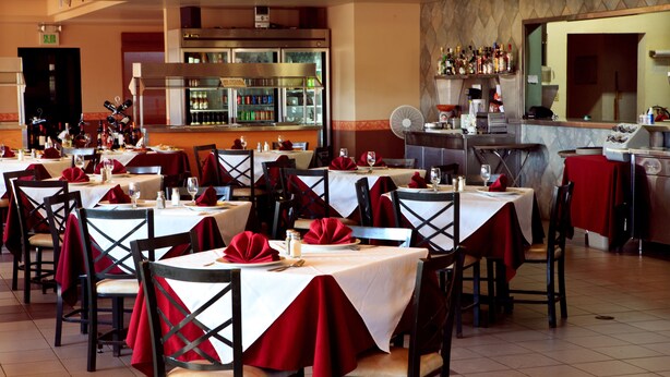 A restaurant with multiple tables, each set with red napkins and white tablecloths.