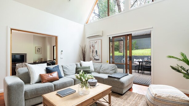 Un salon moderne avec un canapé gris, une table basse en bois et une vue sur un espace patio extérieur.