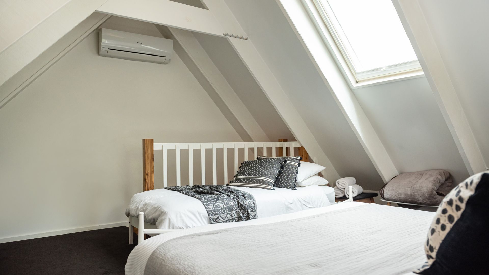 A bedroom with a sloped ceiling, a bed with white bedding, a wooden headboard, and a skylight.