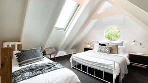 Ein modernes, helles Schlafzimmer im Dachgeschoss mit schrägen Wänden, einem großen Dachfenster und einem runden Fenster, mit einem Bett und einem Kopfteil.