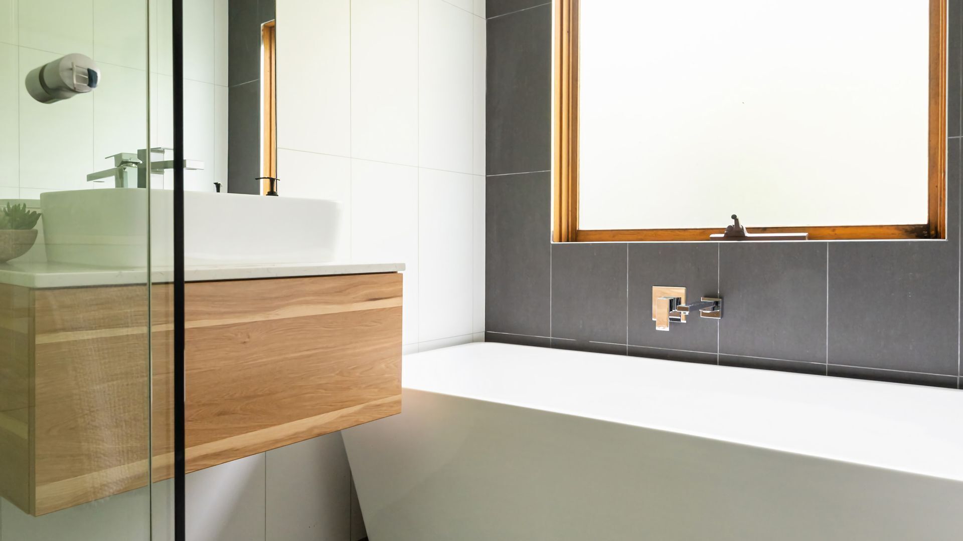 Ein modernes Badezimmer mit einem weißen Waschbecken, einem Holz-Waschtisch und einem großen Spiegel.