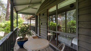 Eine Holzveranda mit Tisch, Stühlen und Blumentöpfen, mit Blick auf die umliegende Grünfläche.