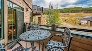Ein Balkon mit Tisch und Stühlen, der auf eine reizvolle Landschaft mit Bäumen und einer entfernten Bergkette blickt.