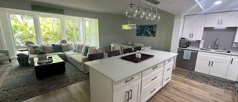 A modern kitchen with white cabinetry, a central island, and a dining area with a sofa and coffee table.