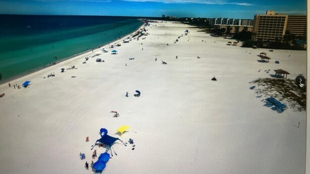 Una spiaggia con cielo sereno, una battigia sabbiosa e edifici sullo sfondo.