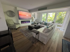 Ein modernes Wohnzimmer mit großem Flachbildfernseher, Kamin, einer Couch und einem Essbereich.