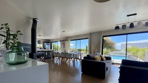 A modern living room with a dining area, a pool, and large windows offering a view of the outdoors. - Villa 12 persons SEA VIEW with CHIMNEY and SAUNA 500m BEACH (Clohars-Carnoët)
