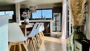 A modern kitchen with a dining area, featuring a large window, wooden flooring, and a decorative vase with pampas grass. - Villa 12 persons SEA VIEW with CHIMNEY and SAUNA 500m BEACH (Clohars-Carnoët)