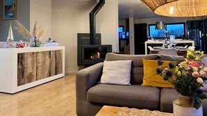 Un salon moderne avec un canapé, une table basse, une cheminée et un coin cuisine à l’arrière-plan.