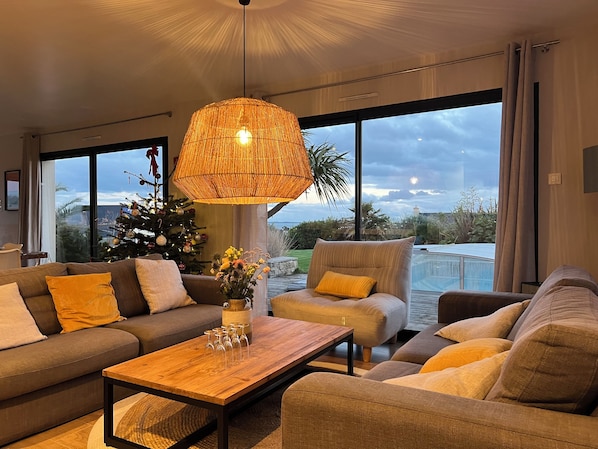 Un salon moderne avec une grande fenêtre, un sapin de Noël et une table basse en bois.
