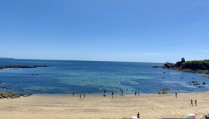 A beach with clear blue water, rocky outcrops, and a lighthouse on a grassy cliff. - Villa 12 persons SEA VIEW with CHIMNEY and SAUNA 500m BEACH (Clohars-Carnoët)