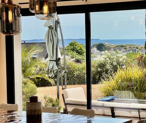 Ein Essbereich mit Tisch, Stühlen und Blick auf das Meer und die grüne Landschaft.