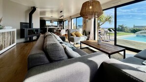 A modern living room with a large sofa, a dining area, and a view of a swimming pool. - Villa 12 persons SEA VIEW with CHIMNEY and SAUNA 500m BEACH (Clohars-Carnoët)