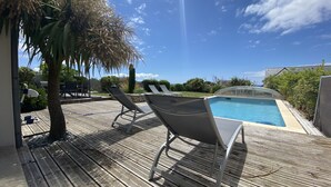 Une terrasse en bois avec une piscine, des chaises longues et un palmier.