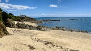 A coastal landscape with a sandy beach, rocky outcrops, and a house on a cliff. - Villa 12 persons SEA VIEW with CHIMNEY and SAUNA 500m BEACH (Clohars-Carnoët)