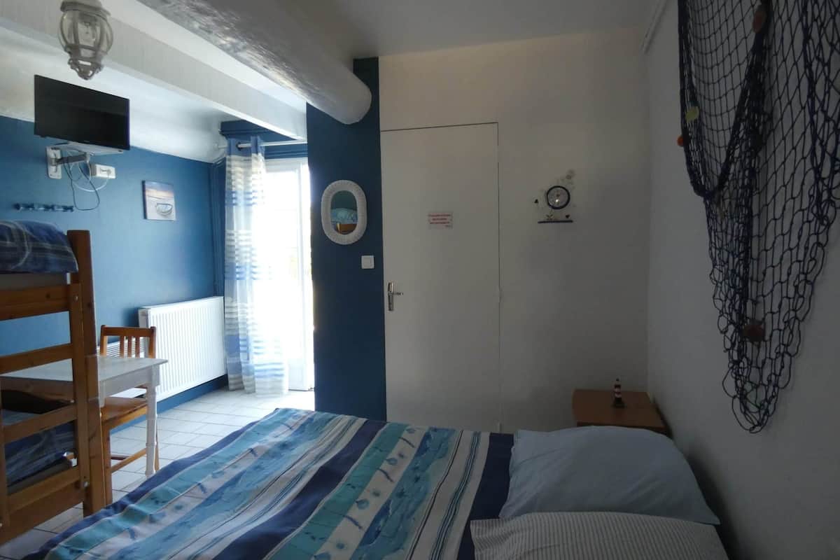 A room with a bunk bed, a desk, a chair, a small table, a wall clock, and a door.