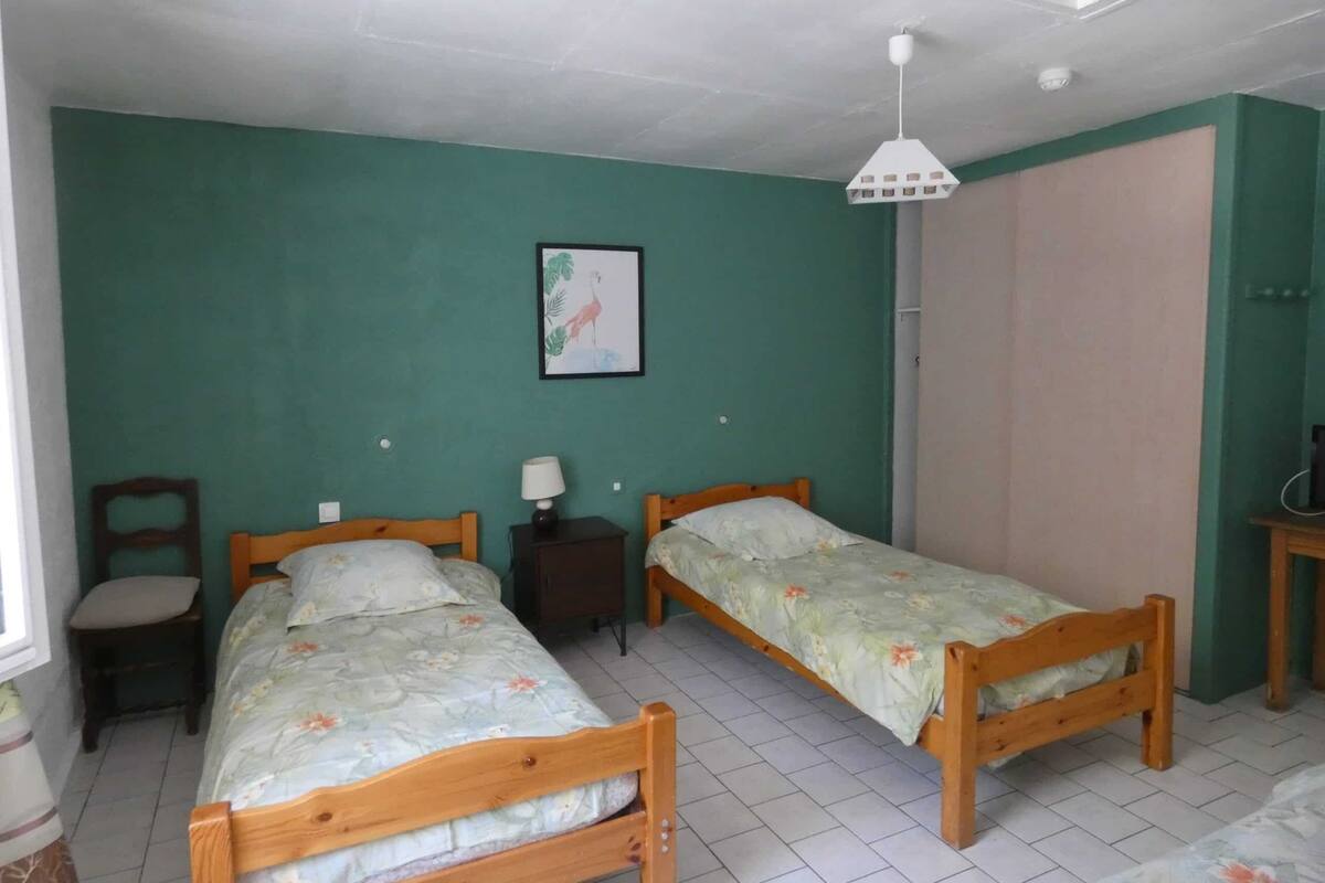 A room with two wooden beds, a chair, a nightstand with a lamp, a framed picture on the wall, and a wardrobe.