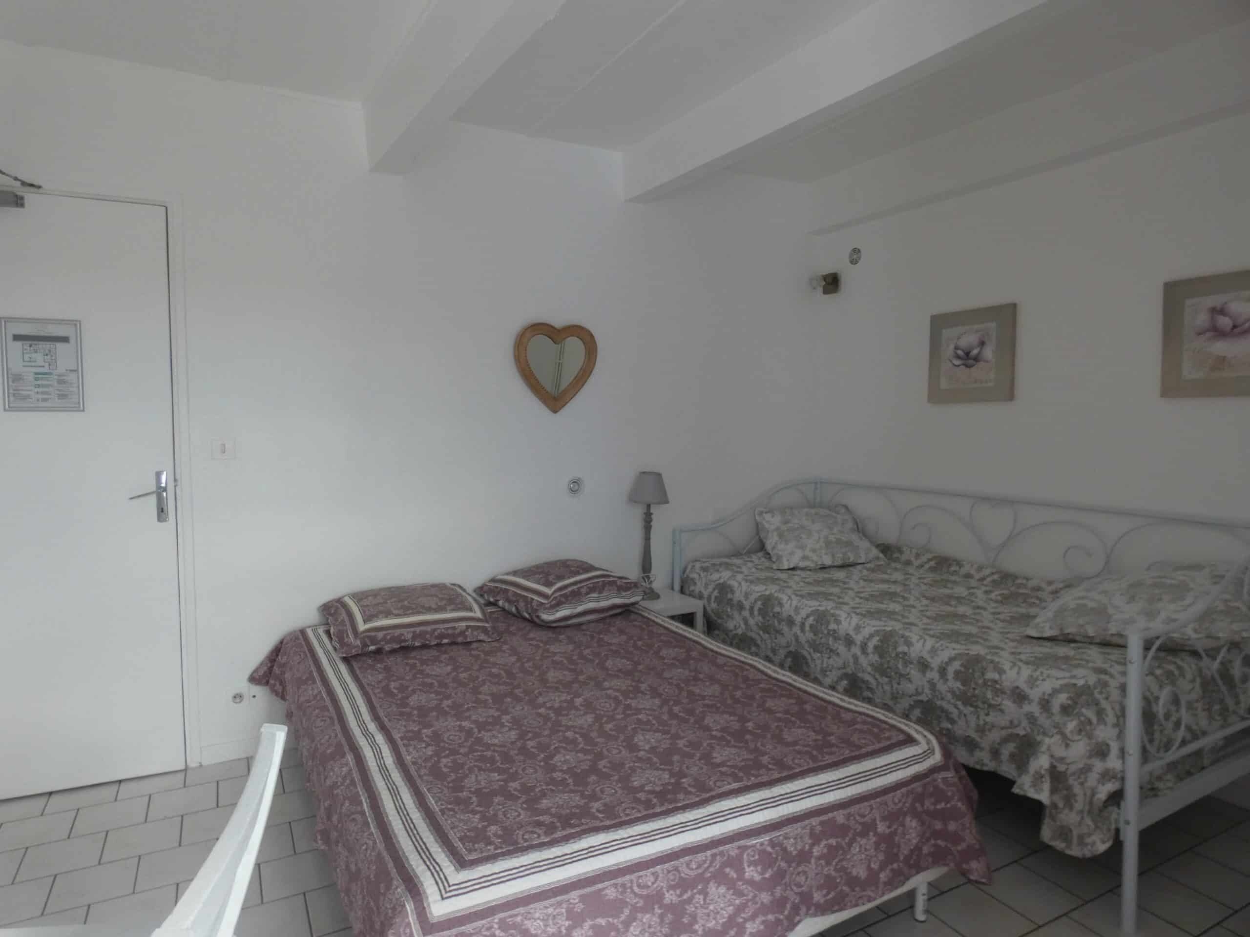 Un dormitorio con dos camas, una puerta blanca, un espejo con forma de corazón y una mesita de noche con una lámpara.