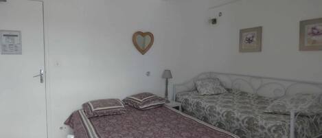 Un dormitorio con dos camas, una puerta blanca, un espejo con forma de corazón y una mesita de noche con una lámpara.