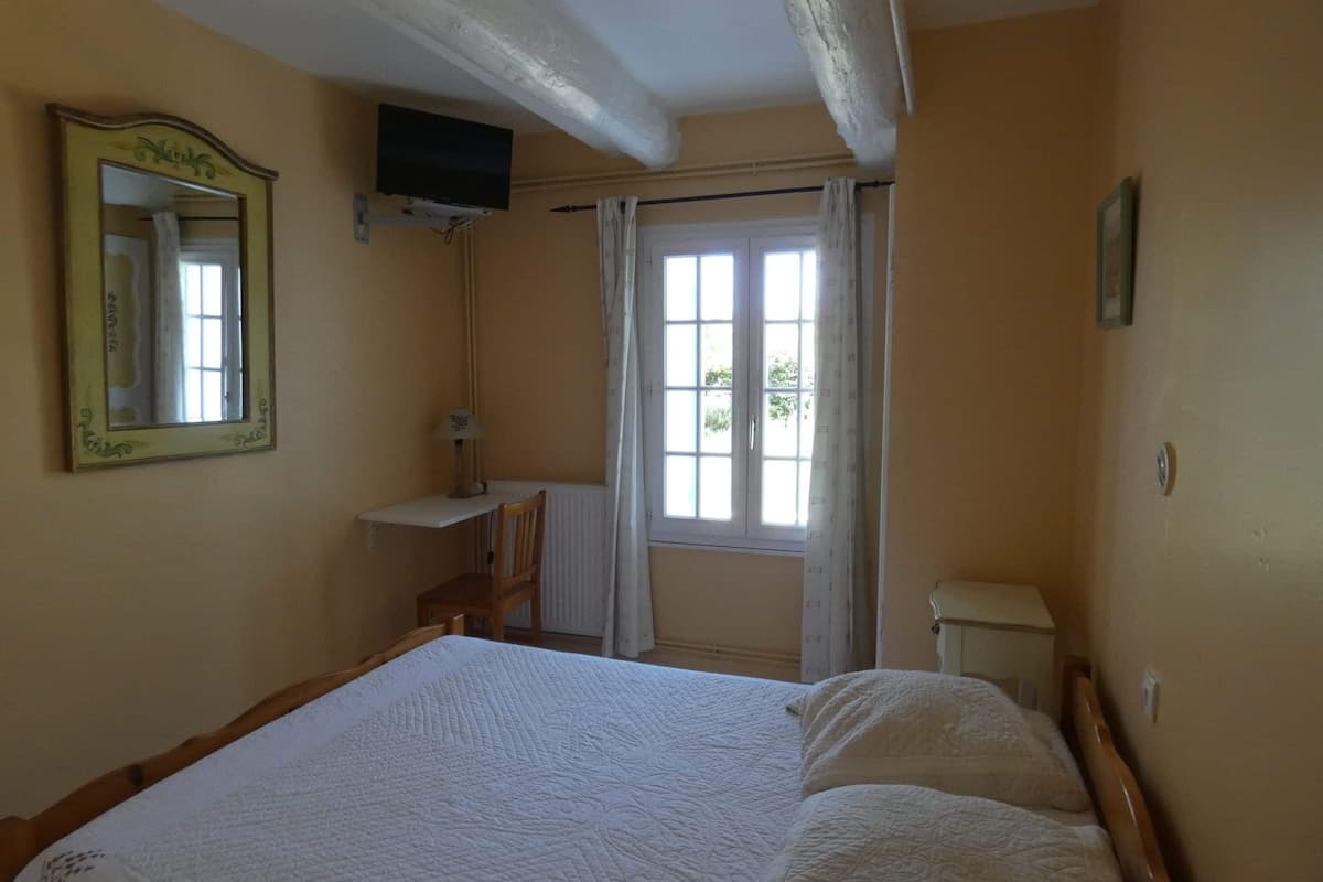 A bedroom with a bed, a desk, a television, and a window with curtains.