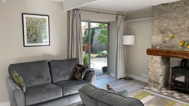 A living room with a grey sofa, a small table, a fireplace, and a view through a glass door. - Bluebell Cottage, Characterful Cottage in the Yorkshire Dales (Langcliffe)