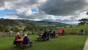 A group of people sitting at wooden picnic tables outdoors with a scenic view of green hills and a cloudy sky. - Bluebell Cottage, Characterful Cottage in the Yorkshire Dales (Langcliffe)