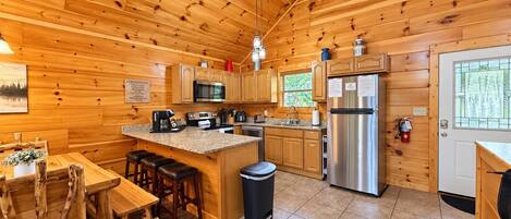 A wooden cabin interior with a kitchen, dining area, and bar stools.