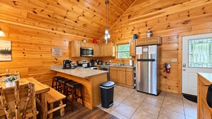 A wooden cabin interior with a kitchen, dining area, and bar stools.