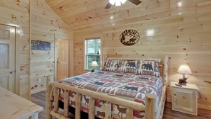 Un dormitorio de cabaña de madera con cama, mesita de noche, ventilador de techo y ventana.