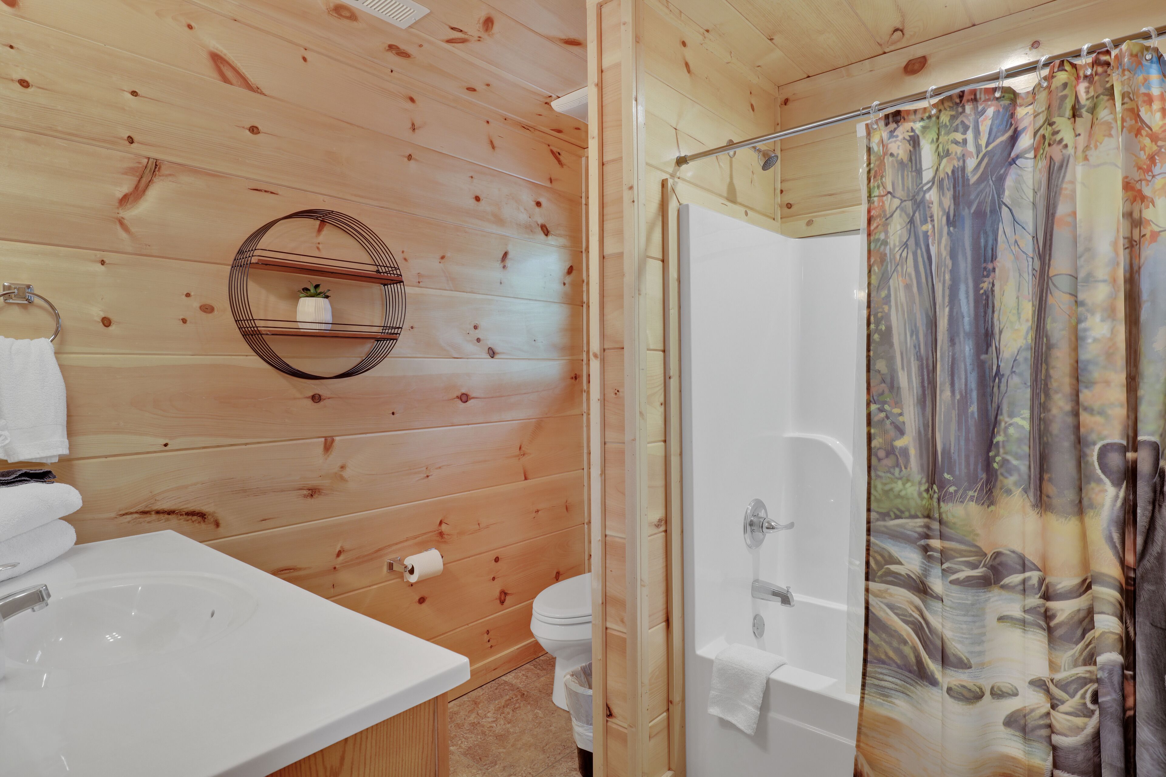 Ein Badezimmer mit Holzwänden, einem weißen Waschbecken, einer Toilette und einer Duschvorhang mit Waldmotiv.