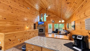 A cozy cabin interior with a stone fireplace, wooden walls, a granite countertop, and a coffee machine.