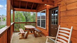 Una terraza de madera con una mesa de picnic y bancos, una silla de madera y una puerta.