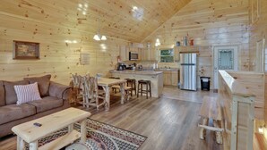 Acogedor interior de cabaña de madera con sala de estar, comedor, cocina y una pequeña isla.