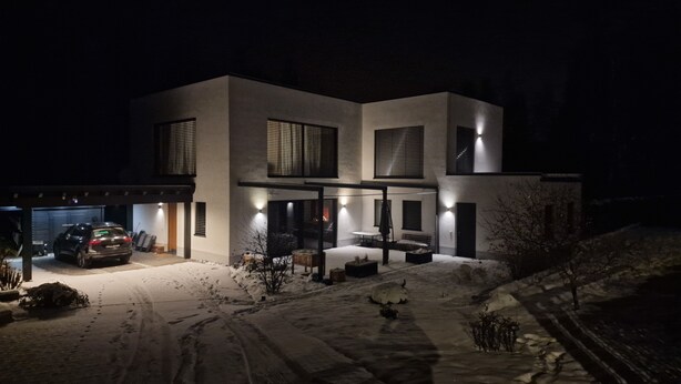 Una casa moderna de dos pisos con garaje, un patio cubierto y un camino de entrada cubierto de nieve.
