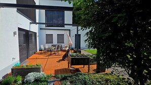 Una casa moderna con terraza de madera, mobiliario exterior y jardín.