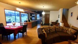 Un salón amplio con suelo de madera, un sofá, una mesa de comedor con sillas y una cocina al fondo.