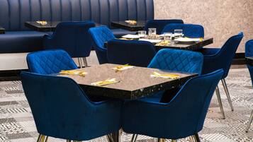 Un restaurante con asientos tapizados en azul y mesas, cada conjunto con cubiertos y vasos.