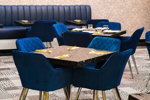 Un restaurante con asientos tapizados en azul y mesas, cada conjunto con cubiertos y vasos.