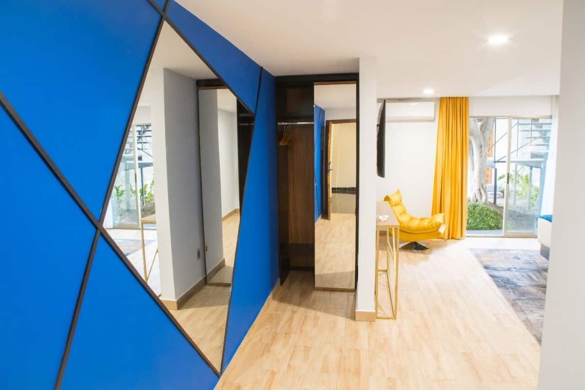 A modern hotel room with a wooden floor, a yellow chair, and a large window with yellow curtains.