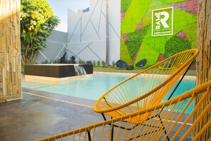 Zona de piscina con una silla amarilla, una cascada y una pared colorida con un logo.