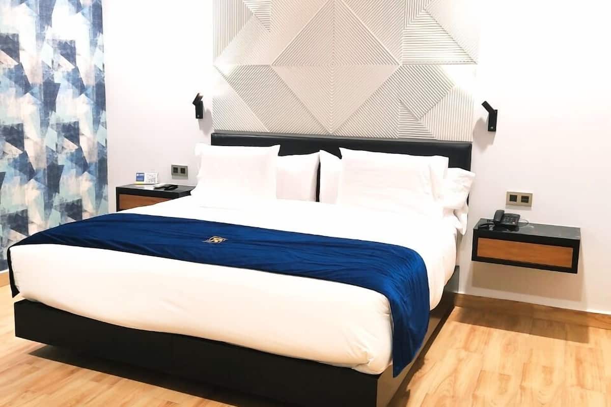 A modern bedroom with a large bed, a geometric wall design, and a wooden floor.