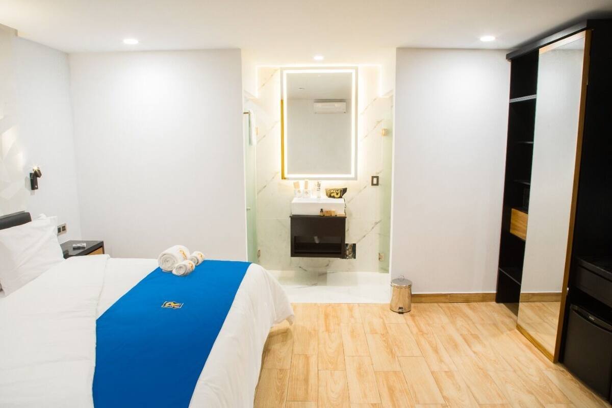 A hotel room with a bed, a blue bedspread, a mirror, a sink, and a wardrobe.