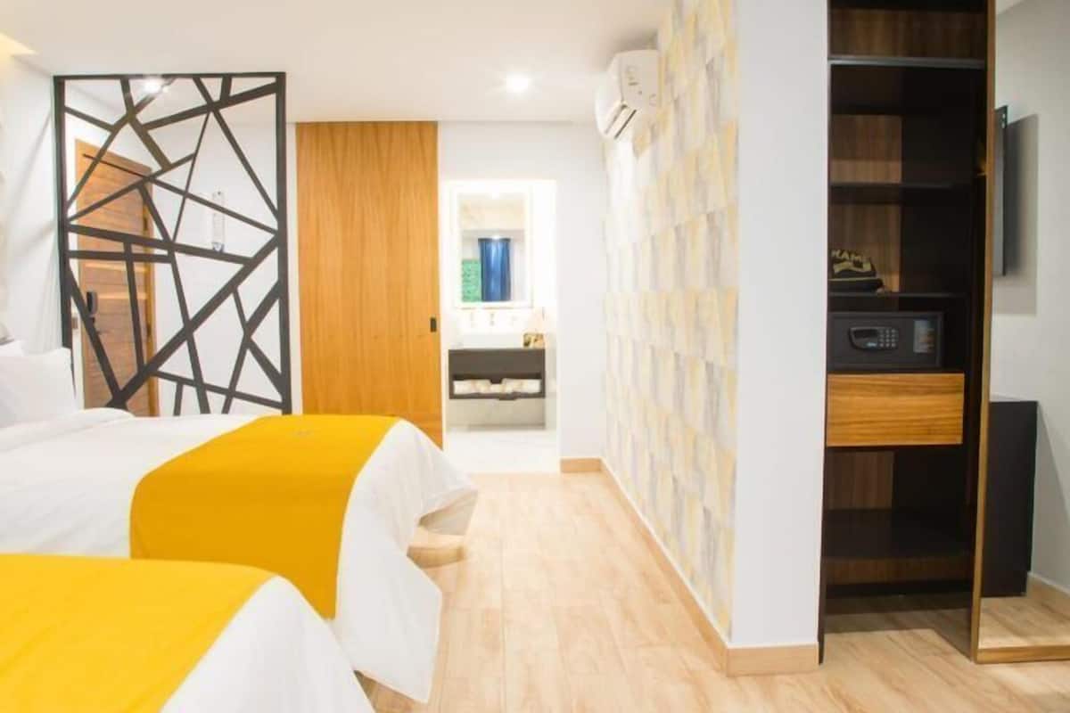 A hotel room with two beds, a wooden floor, a wardrobe, and a bathroom visible through an open door.