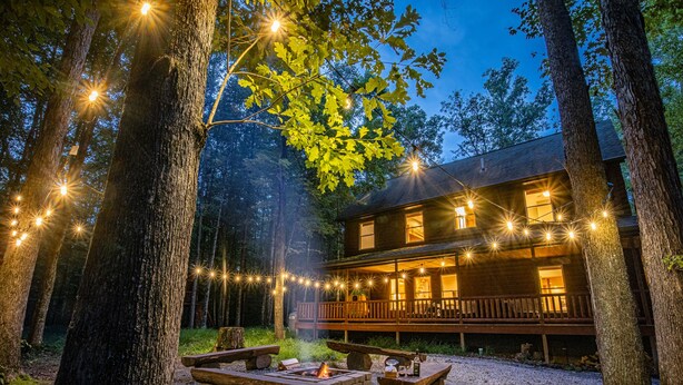 Une cabane dotée d’une terrasse, entourée d’arbres, et illuminée de guirlandes lumineuses.