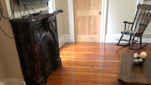 Une pièce dotée d’un plancher en bois, d’une cheminée, d’une table à manger agrémentée d’objets décoratifs et d’un fauteuil à bascule.