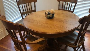 Une table de salle à manger ronde en bois, entourée de quatre chaises en bois. Un panier tressé contenant des objets décoratifs est posé sur la table.